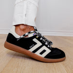 Black Adidas sneaker with white accents on a wooden floor