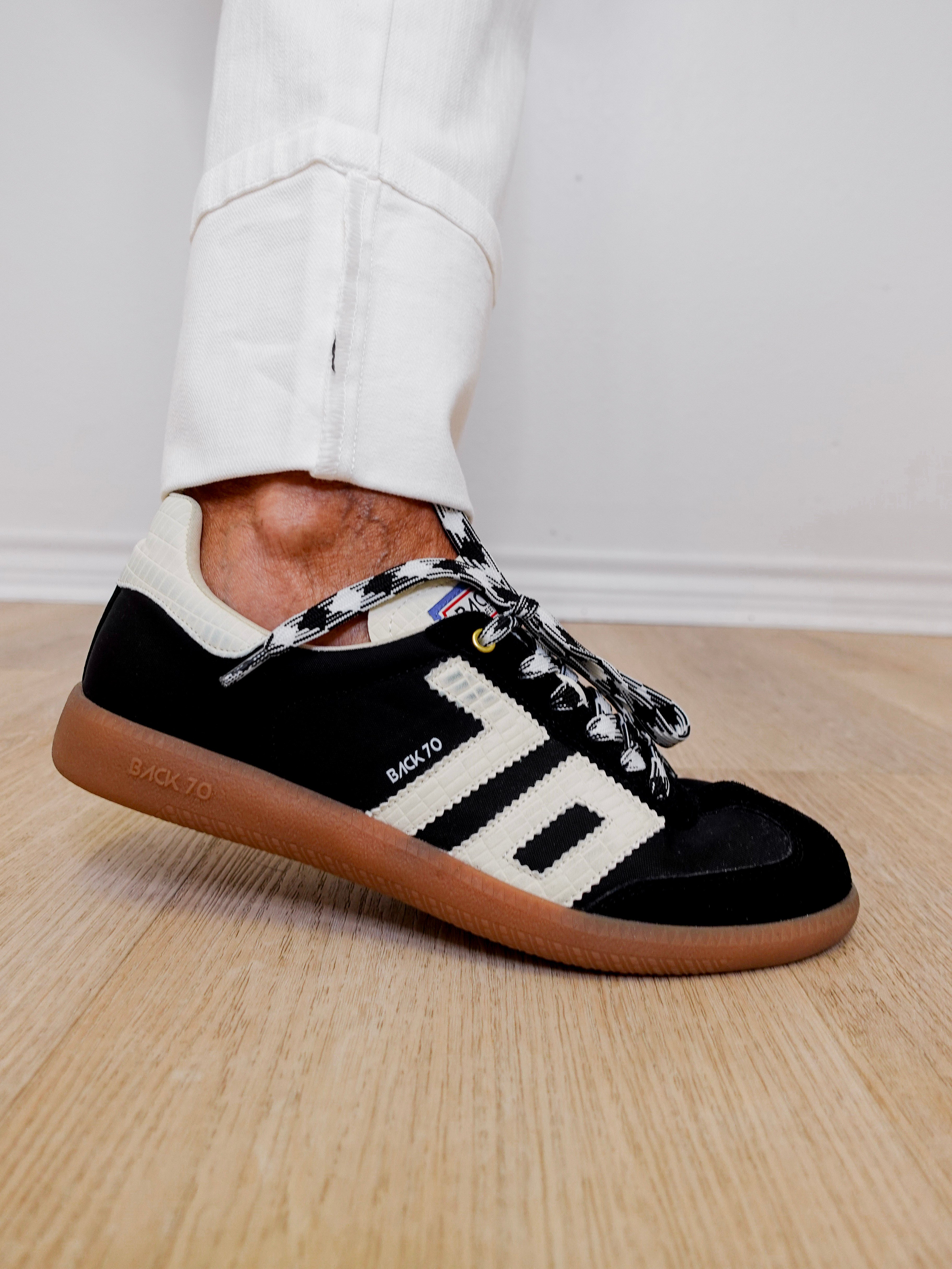 Black Adidas sneaker with white accents on a wooden floor