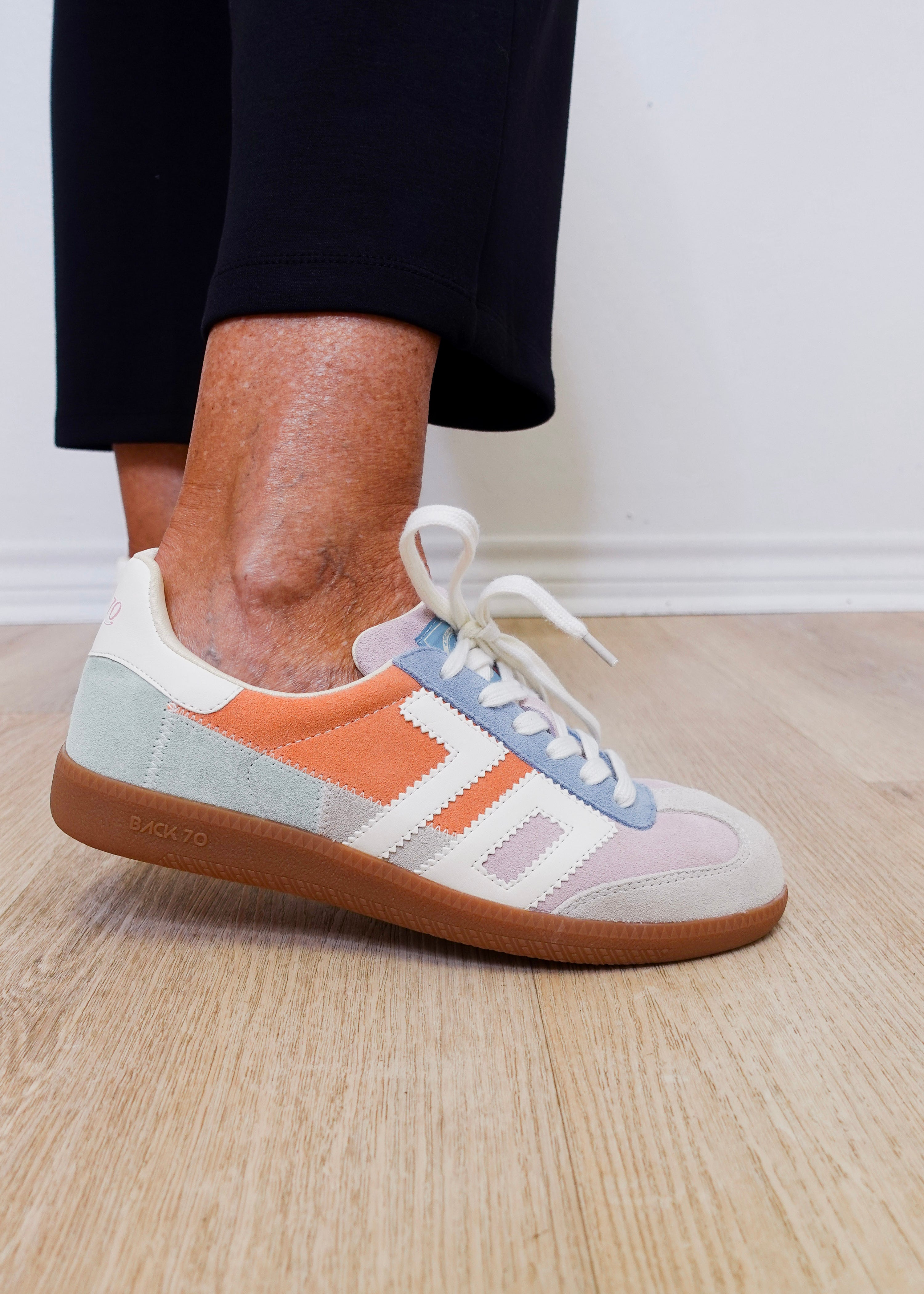 Multicolored sneaker with white laces worn indoors on a wooden floor.