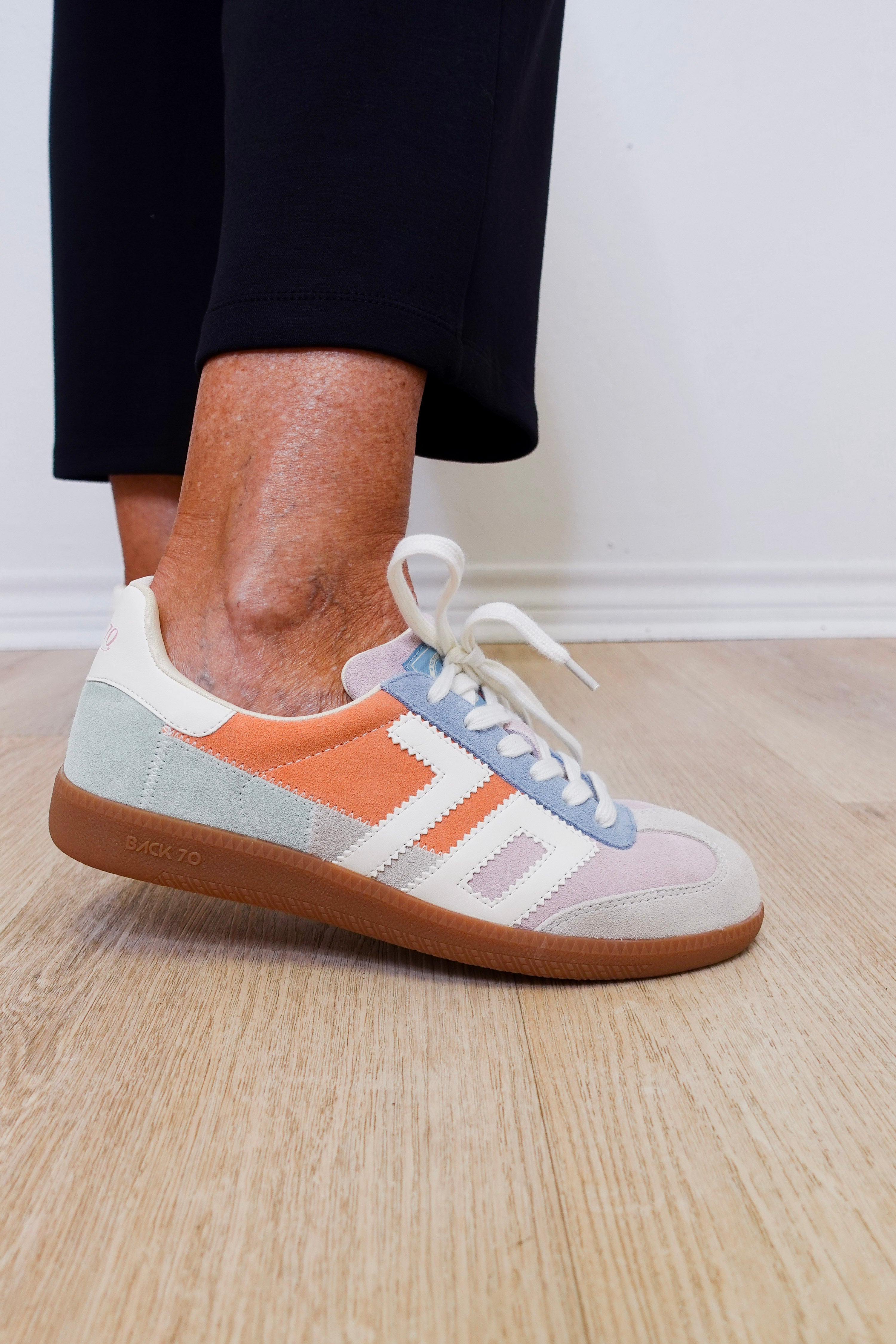 Multicolored sneaker with white laces worn indoors on a wooden floor.