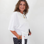 Woman wearing a white top and black patterned pants against a white background