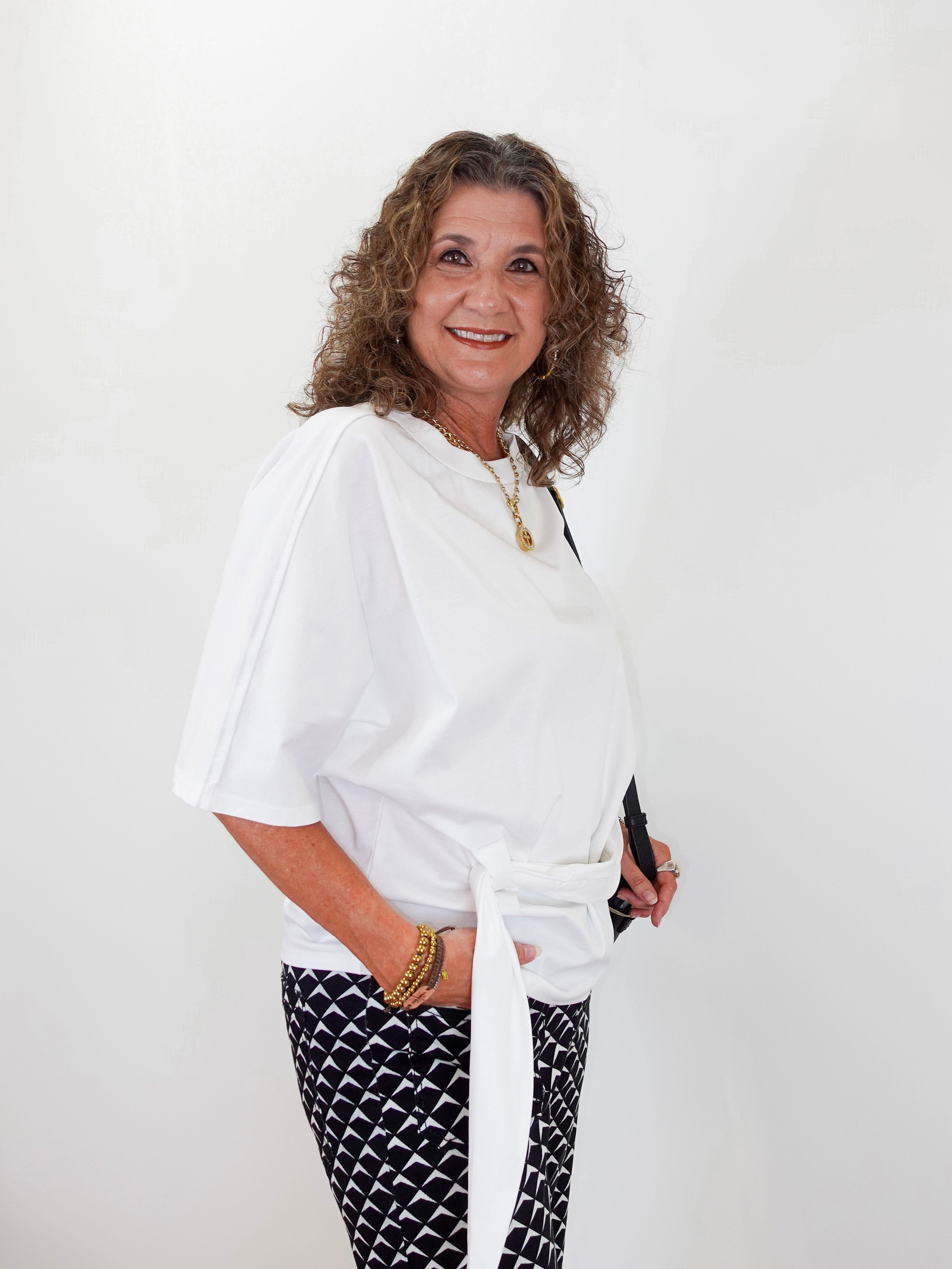 Woman wearing a white top and black patterned pants against a white background
