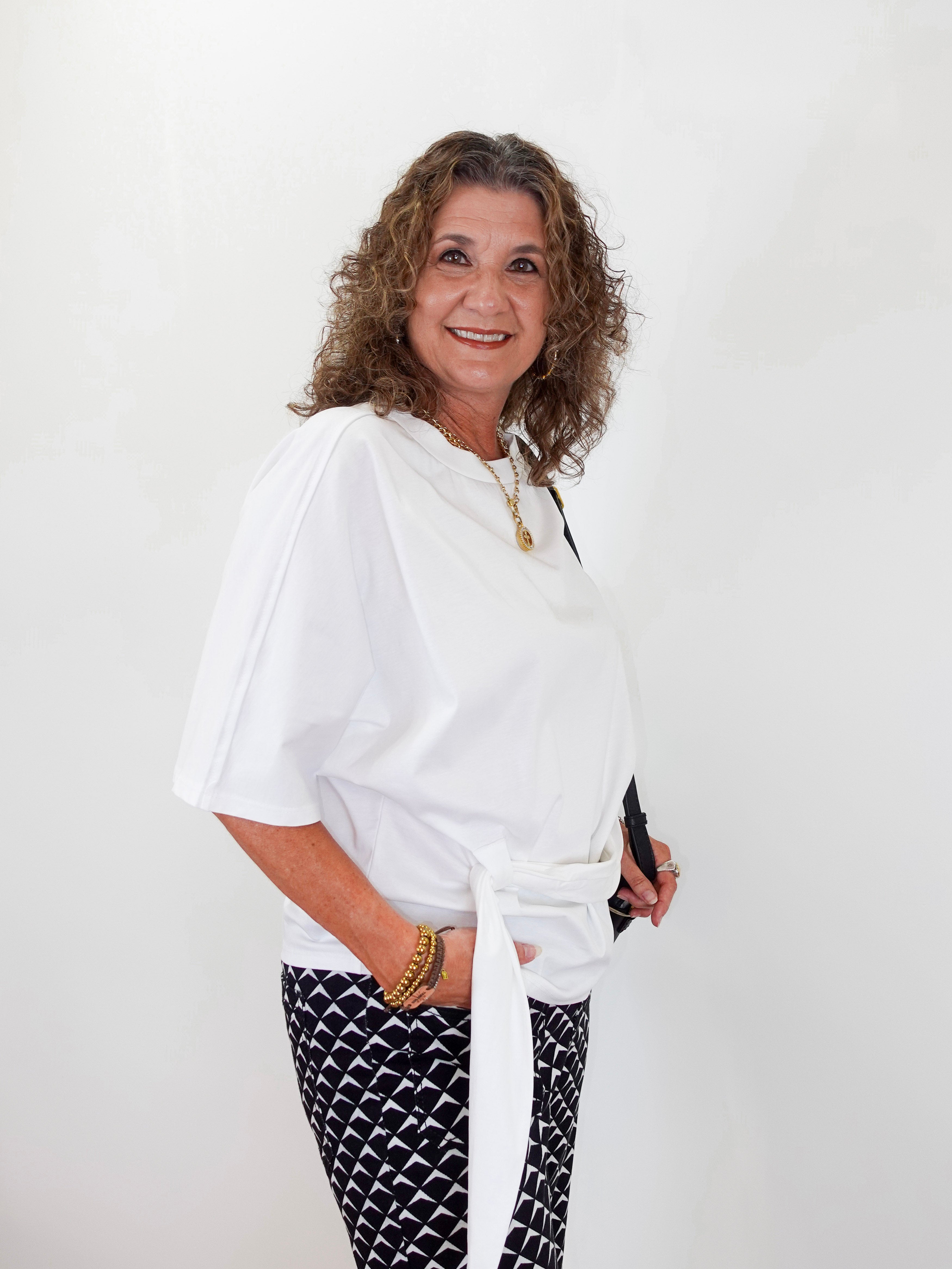 Woman wearing a white top and black patterned pants against a white background