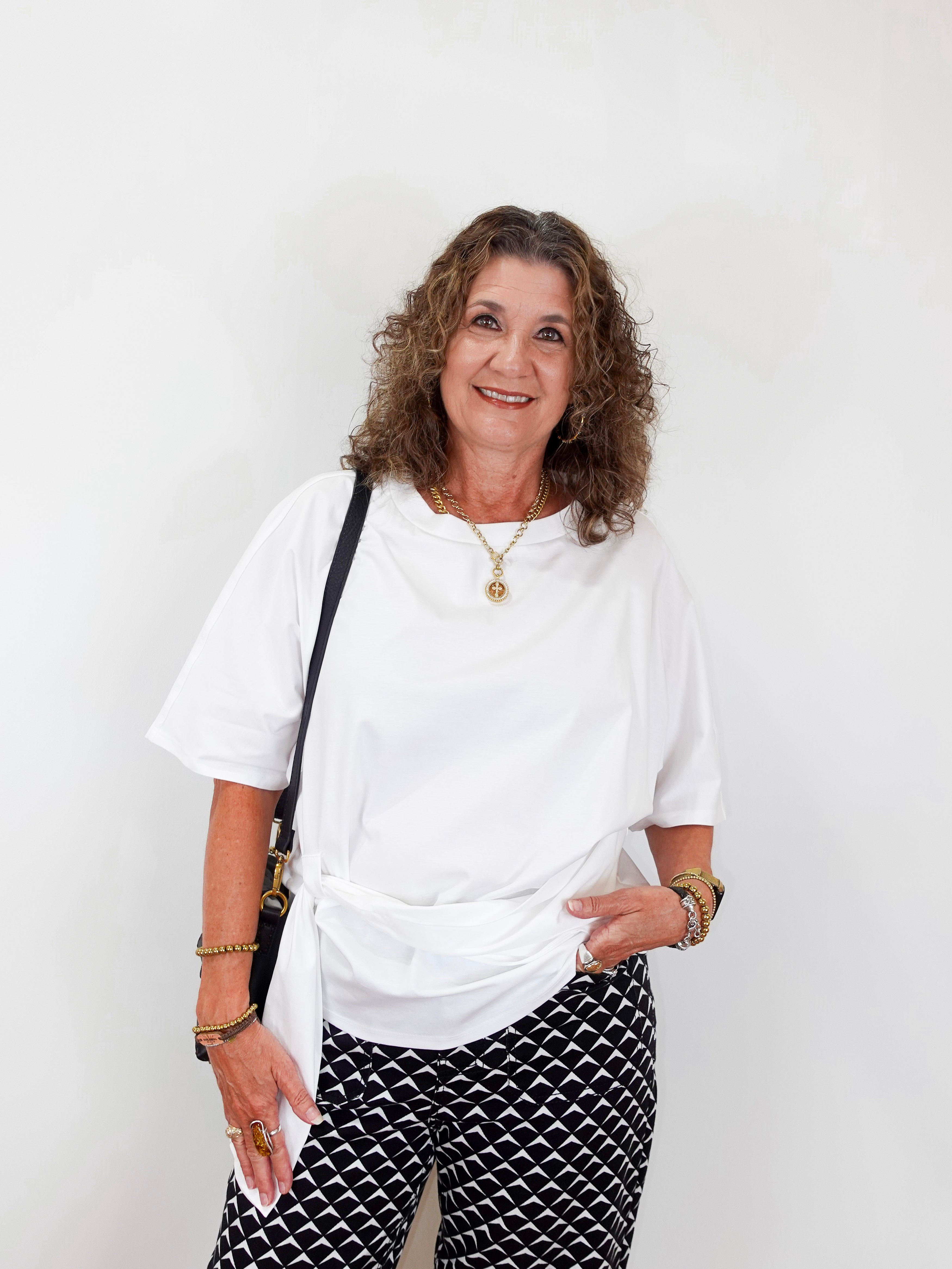 Woman wearing a white top and patterned pants against a plain background