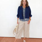 Woman wearing a blue jacket and beige pants against a white wall.
