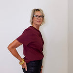 Person wearing a burgundy shirt and black pants against a white wall