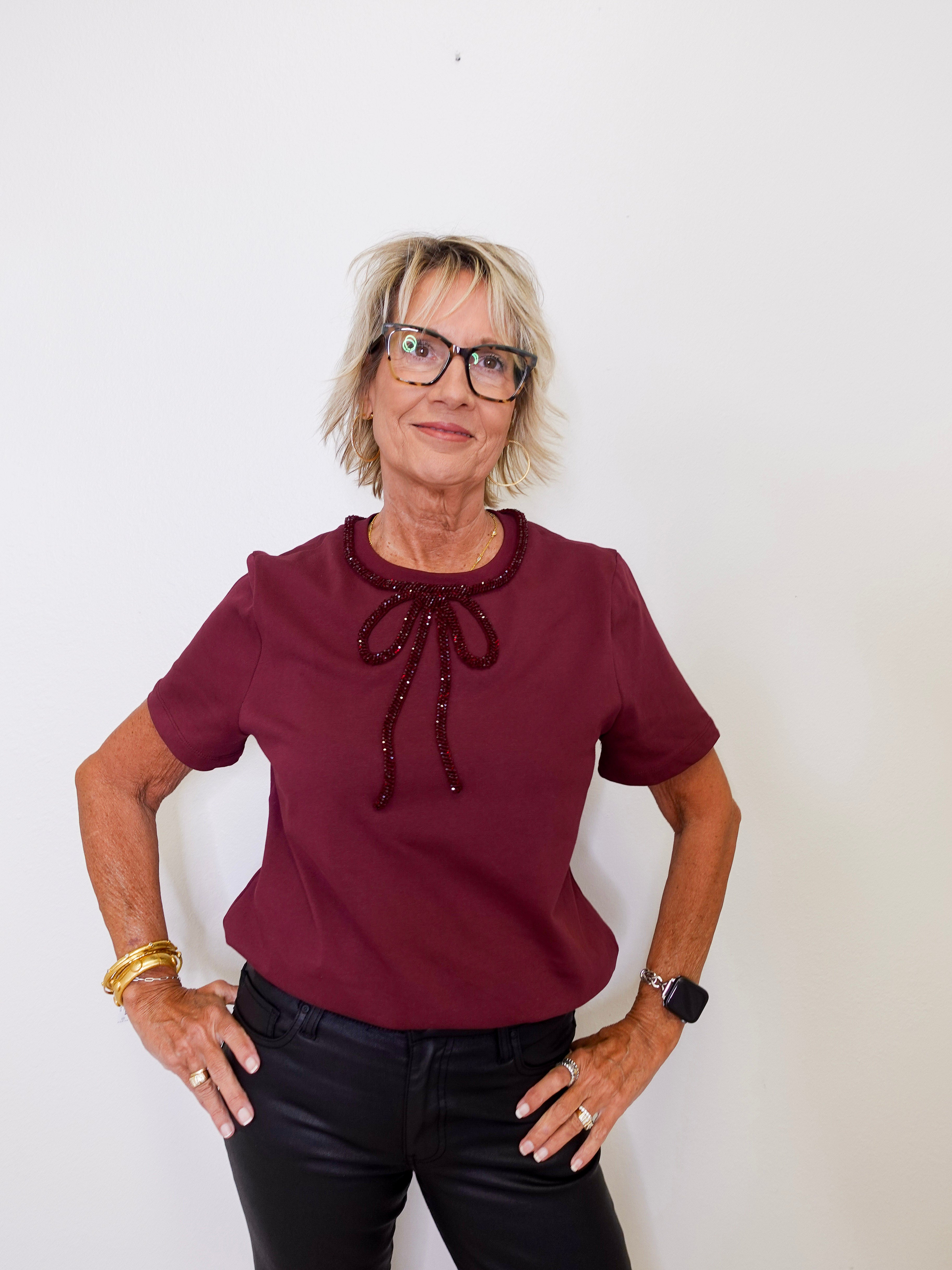 Woman wearing a burgundy blouse with a decorative bow and black pants against a white background