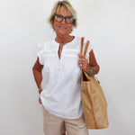 Woman wearing a white blouse and beige shorts, holding a straw bag against a white background