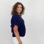 Woman wearing a navy blue top and white pants against a plain background