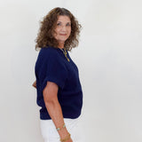 Woman wearing a navy blue top and white pants against a plain background