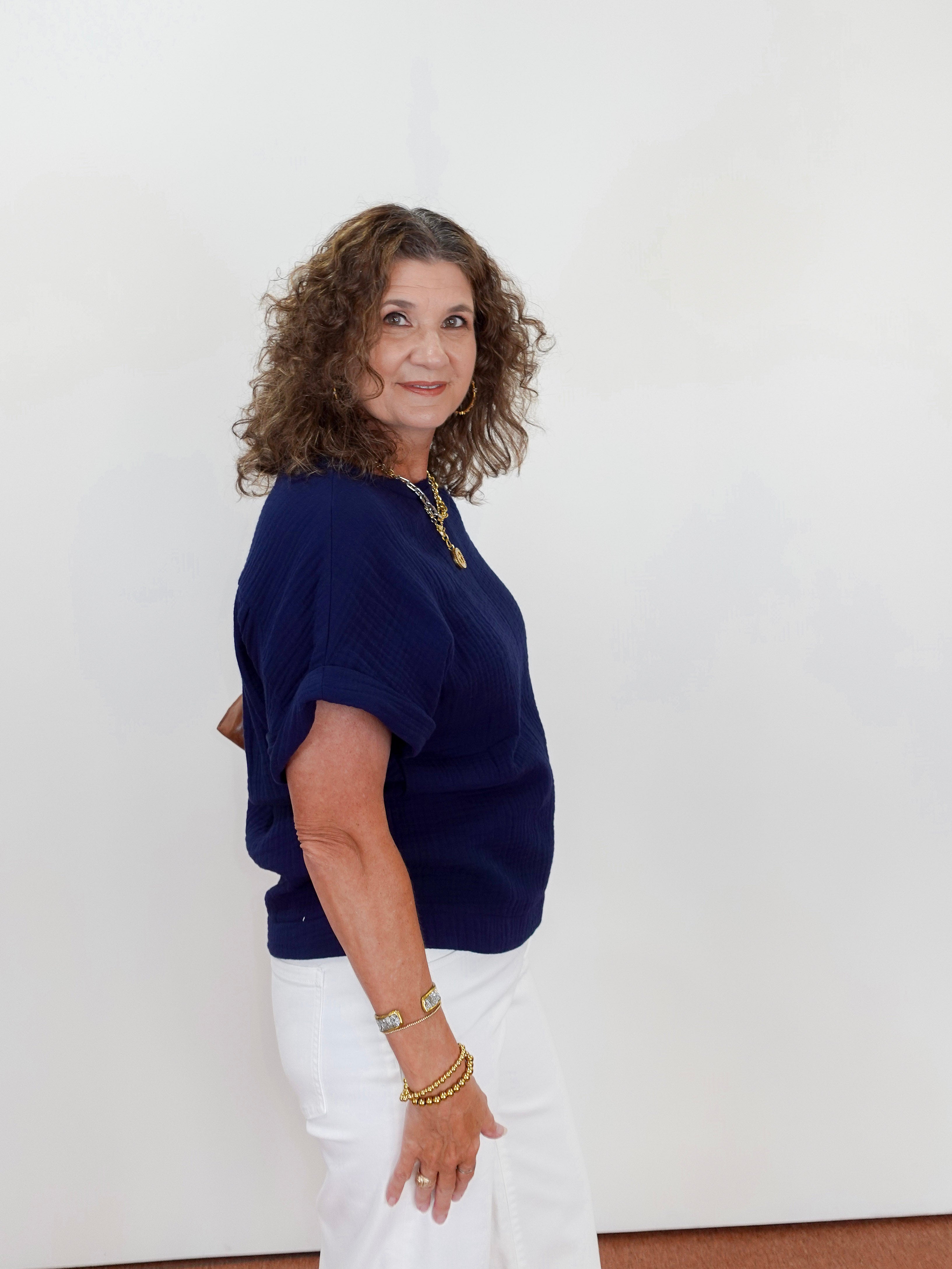 Woman wearing a navy blue top and white pants against a plain background