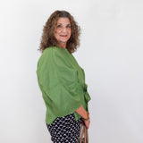 Woman wearing a green top and patterned pants holding a beige handbag against a white background
