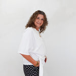 Woman wearing a white blouse and black patterned pants against a plain background