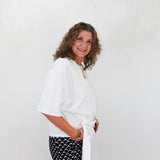 Woman wearing a white blouse and black patterned pants against a plain background