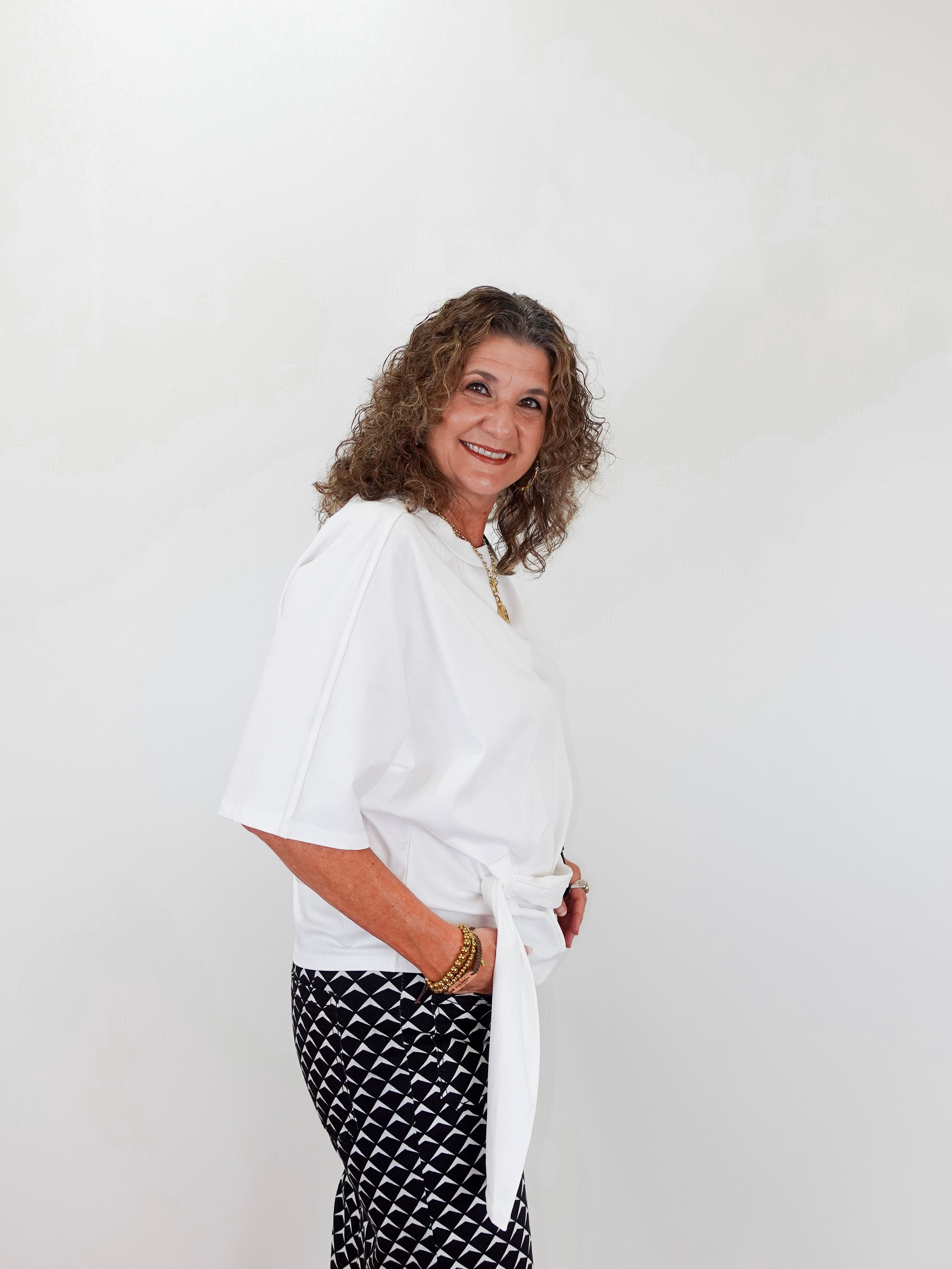 Woman wearing a white blouse and black patterned pants against a plain background
