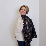 Person wearing a floral lace jacket over a white sweater against a plain background
