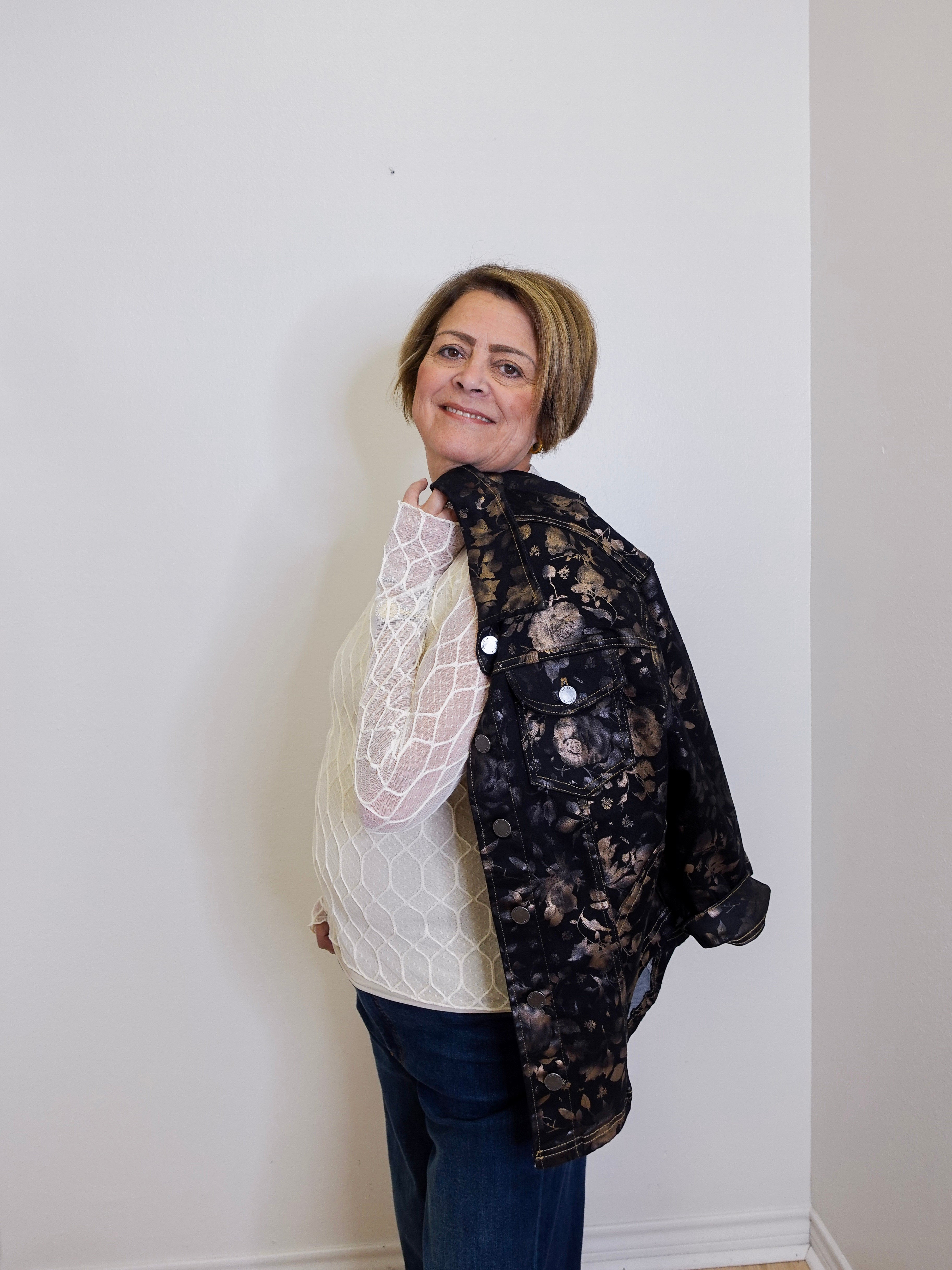 Person wearing a floral lace jacket over a white sweater against a plain background
