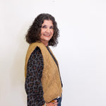 Woman wearing a beige quilted jacket over a leopard print shirt against a white background