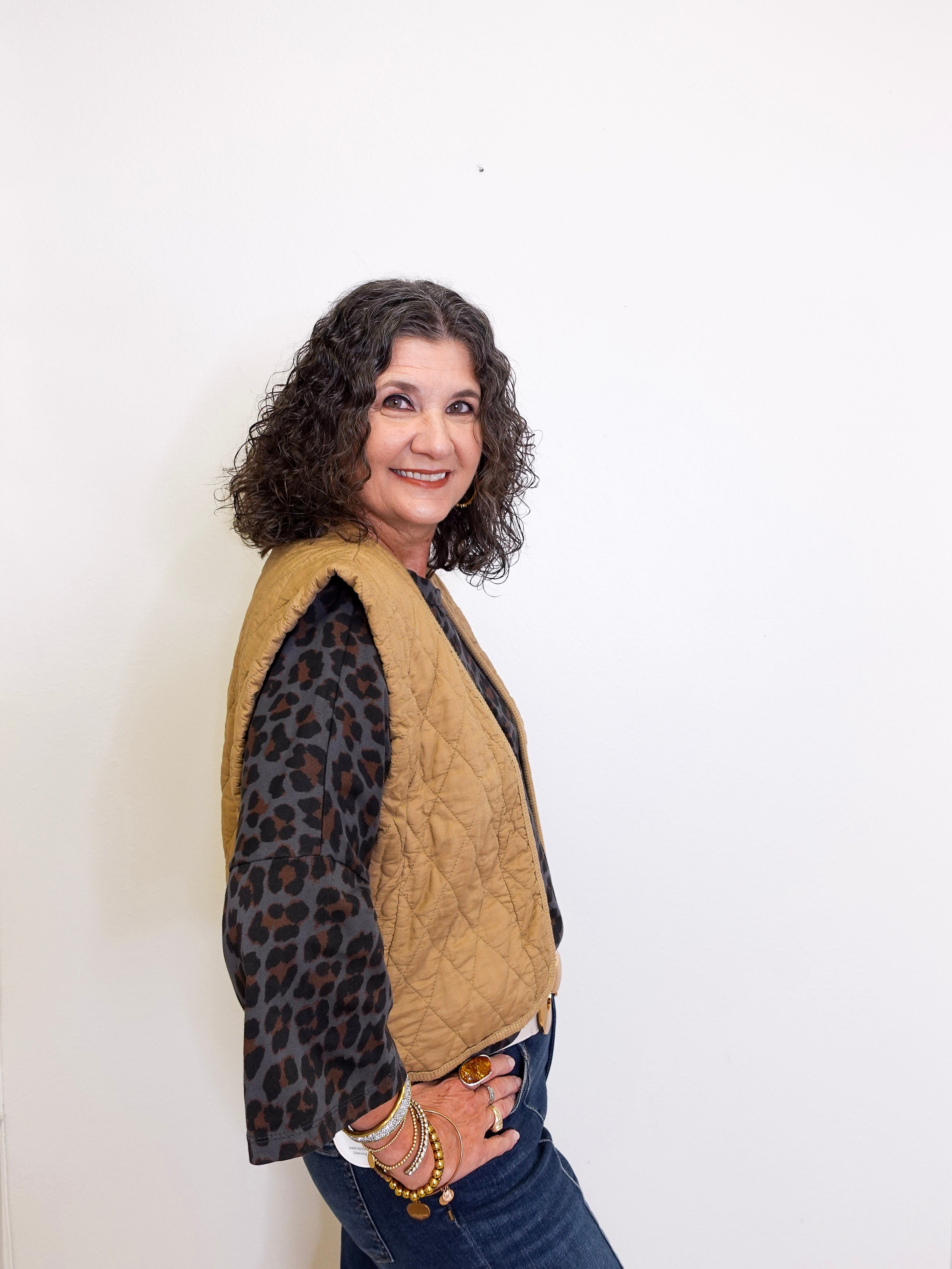 Woman wearing a beige quilted jacket over a leopard print shirt against a white background