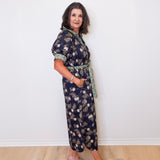 Woman wearing a floral dress standing against a white wall.