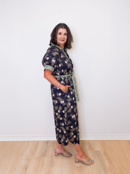 Woman wearing a floral dress standing against a white wall.