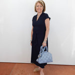Woman in a black dress holding a light blue handbag against a white wall.