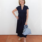 Woman in a navy dress holding a blue handbag against a white wall.