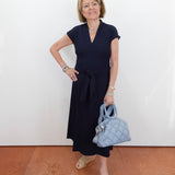 Woman in a navy dress holding a blue handbag against a white wall.