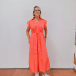 Woman wearing a bright orange dress with vertical stripes against a white wall.