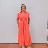 Woman wearing a bright orange dress with vertical stripes against a white wall.