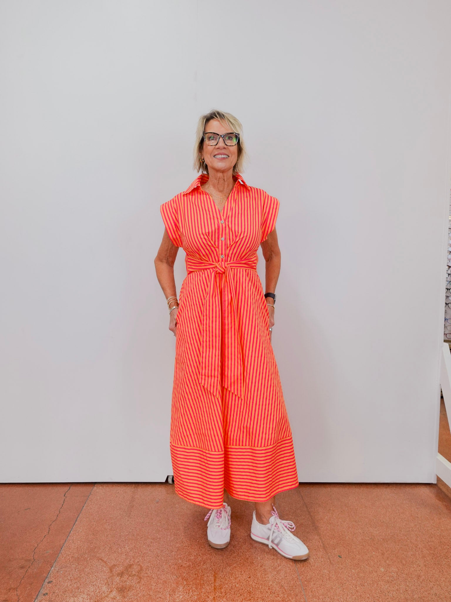 Woman wearing a bright orange dress with vertical stripes against a white wall.
