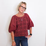 Woman wearing a burgundy blouse with geometric pattern and blue jeans against a white background