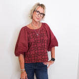 Woman wearing a burgundy blouse with geometric pattern and blue jeans against a white background