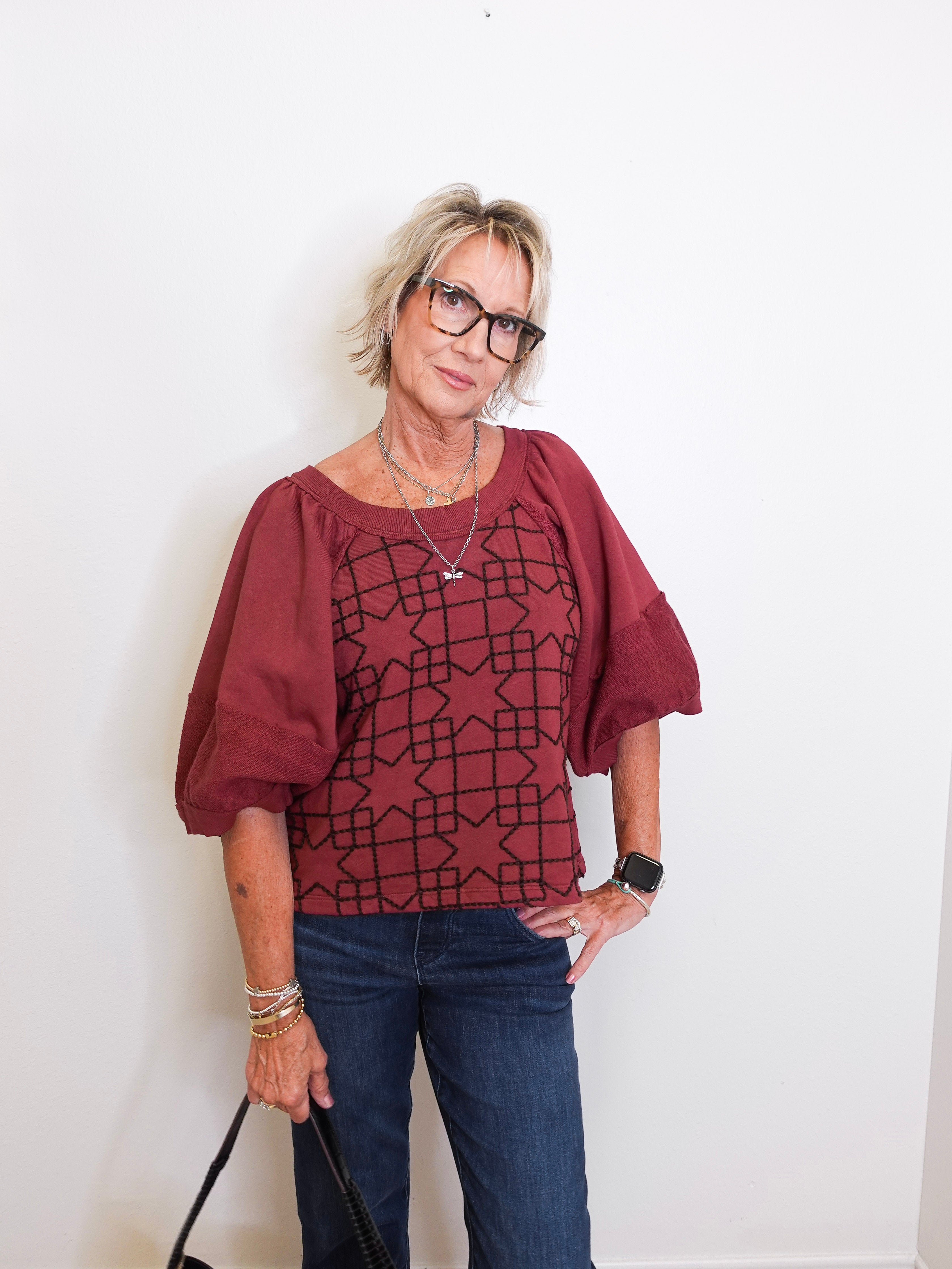 Woman wearing a burgundy blouse with geometric pattern and blue jeans against a white background