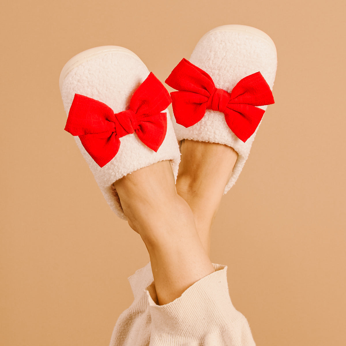 White slippers with red bows worn by a person on a beige background