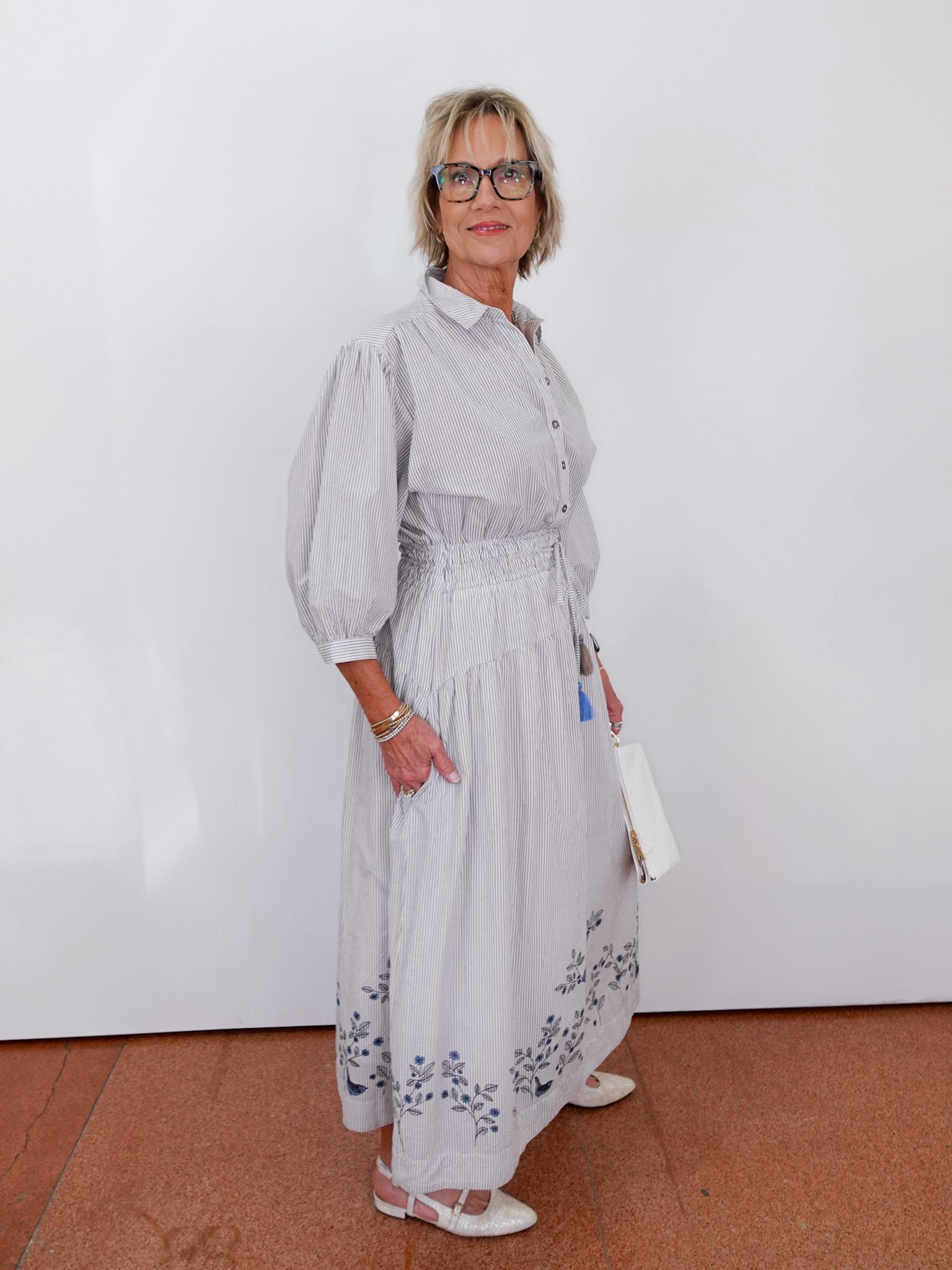 Woman wearing a light gray dress with floral patterns against a white wall.