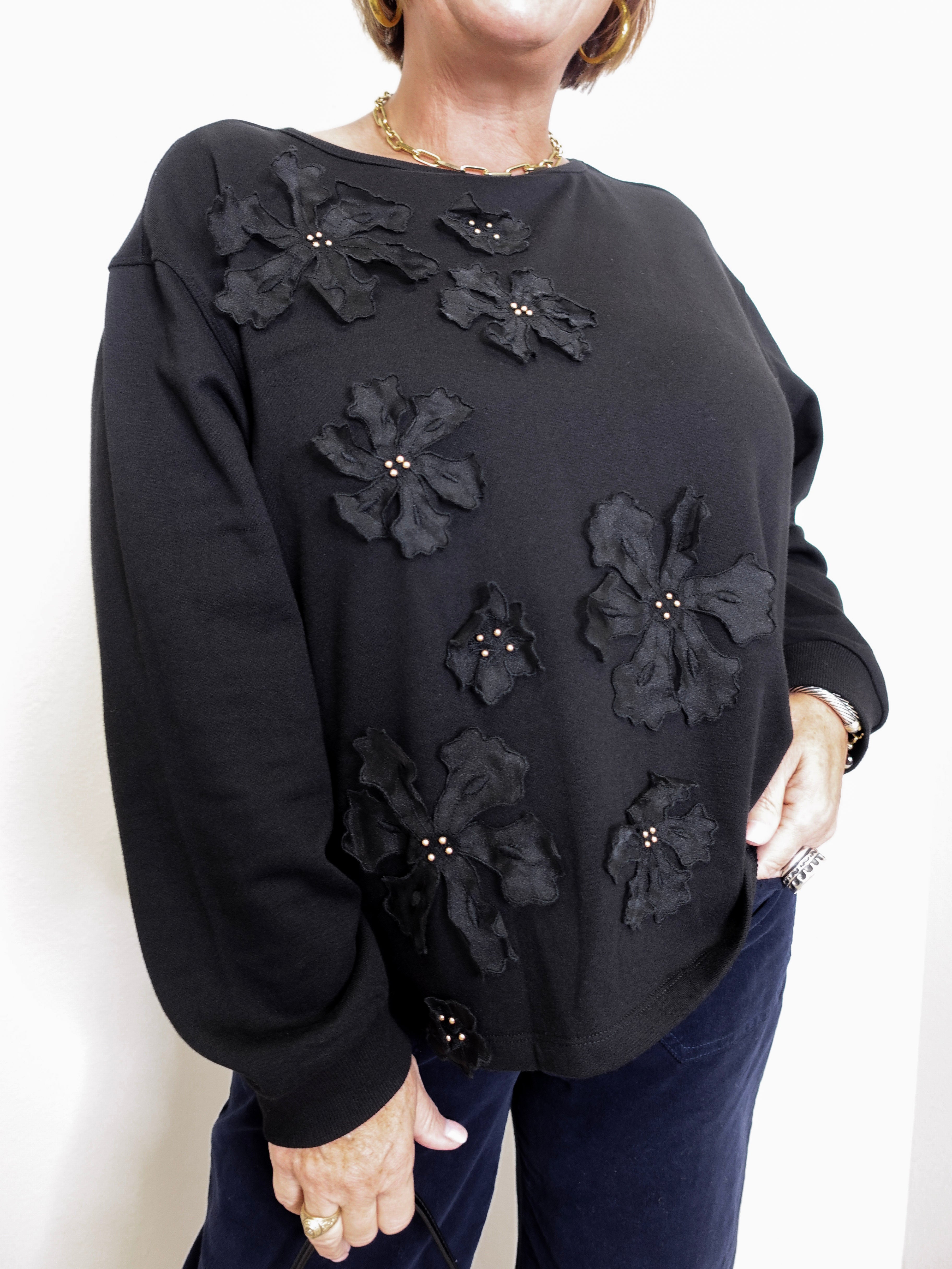 Black sweater with floral embellishments worn by a person on a white background