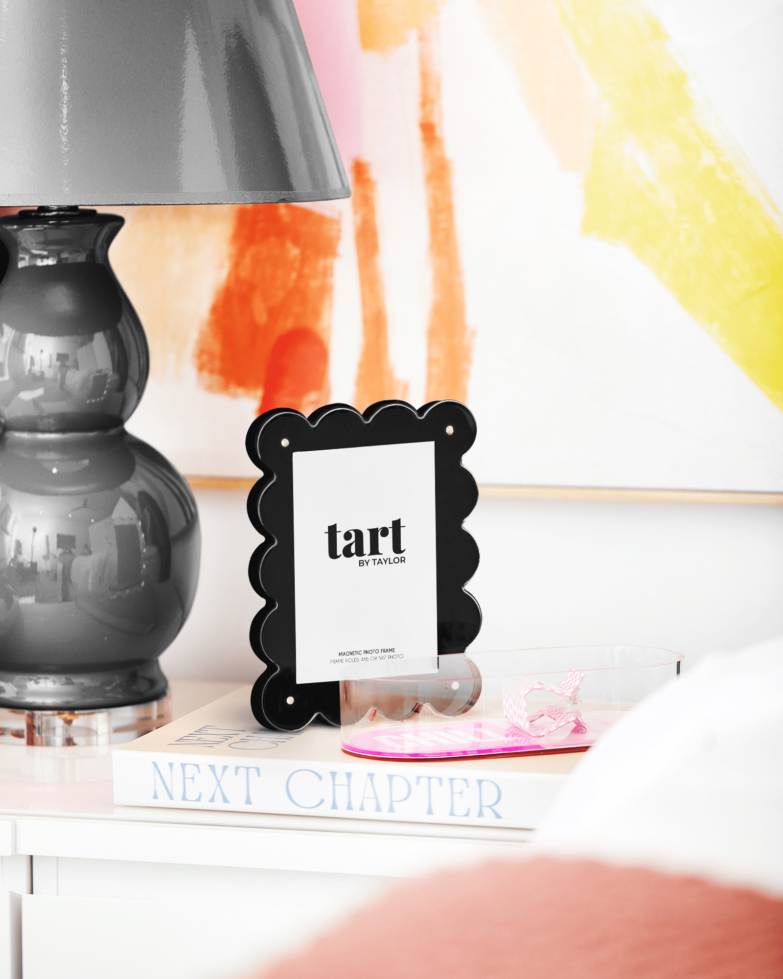 Black scalloped photo frame with 'tart' branding on a shelf with books and a lamp.
