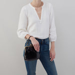 Person wearing a white sweater and blue jeans holding a black handbag against a gray background