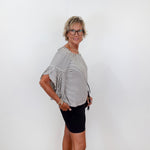 Woman wearing a black and white striped shirt and black shorts against a white wall.