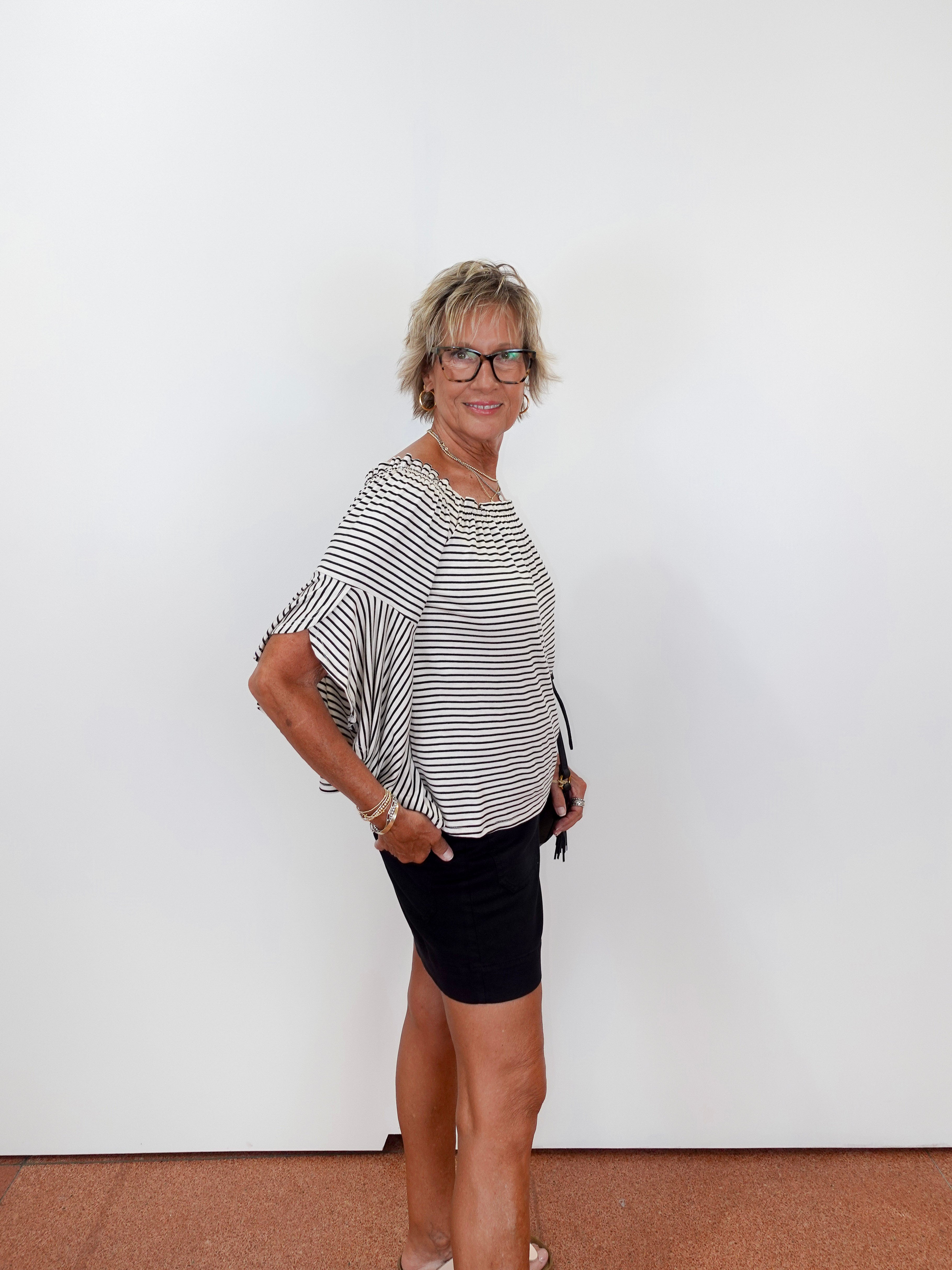 Woman wearing a black and white striped shirt and black shorts against a white wall.
