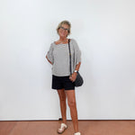 Woman standing against a white wall wearing a striped shirt and black shorts.