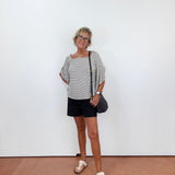Woman standing against a white wall wearing a striped shirt and black shorts.