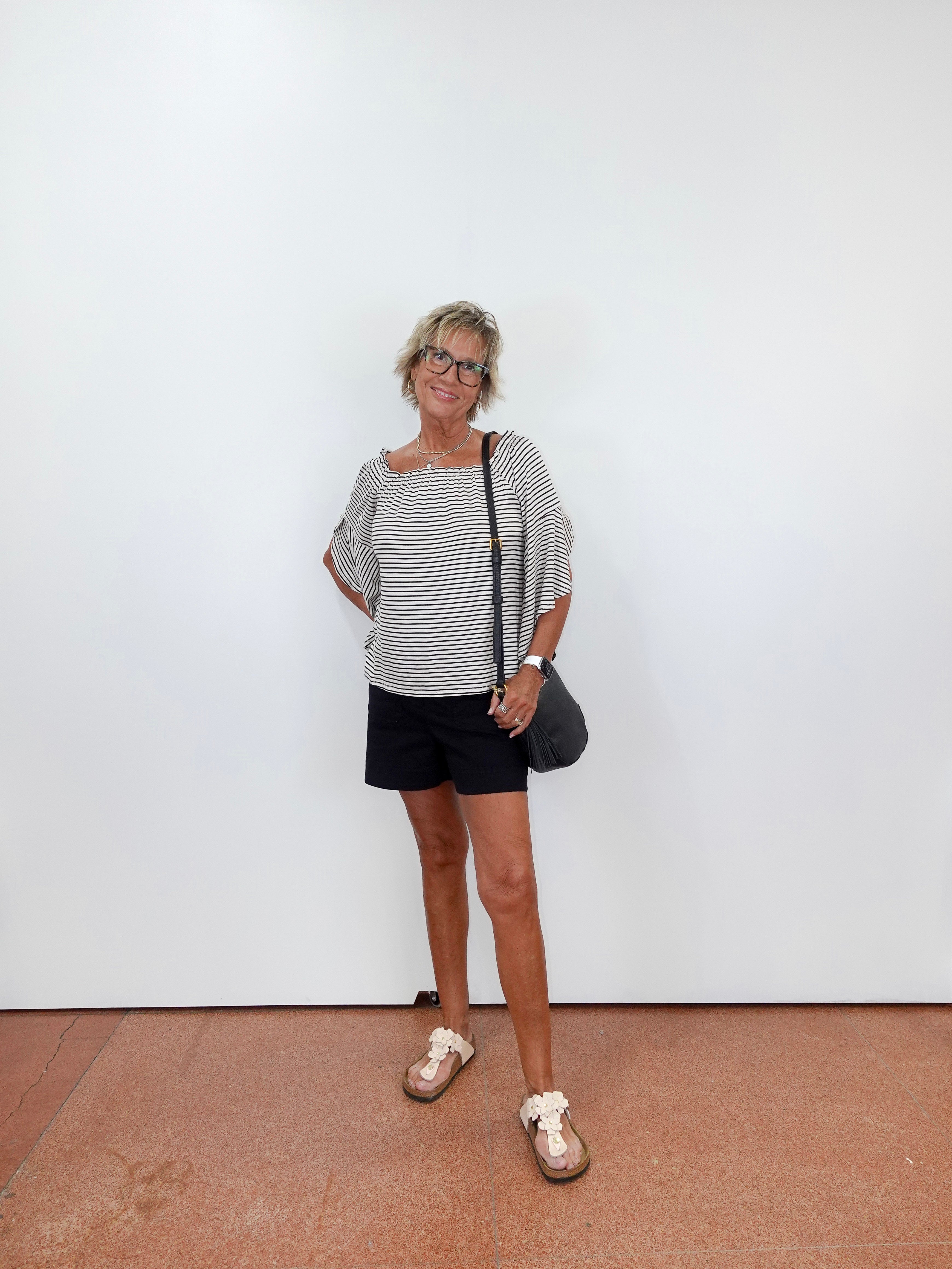 Woman standing against a white wall wearing a striped shirt and black shorts.