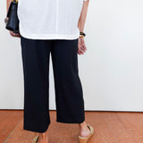 Person wearing a white shirt, black pants, and beige sandals on a plain background