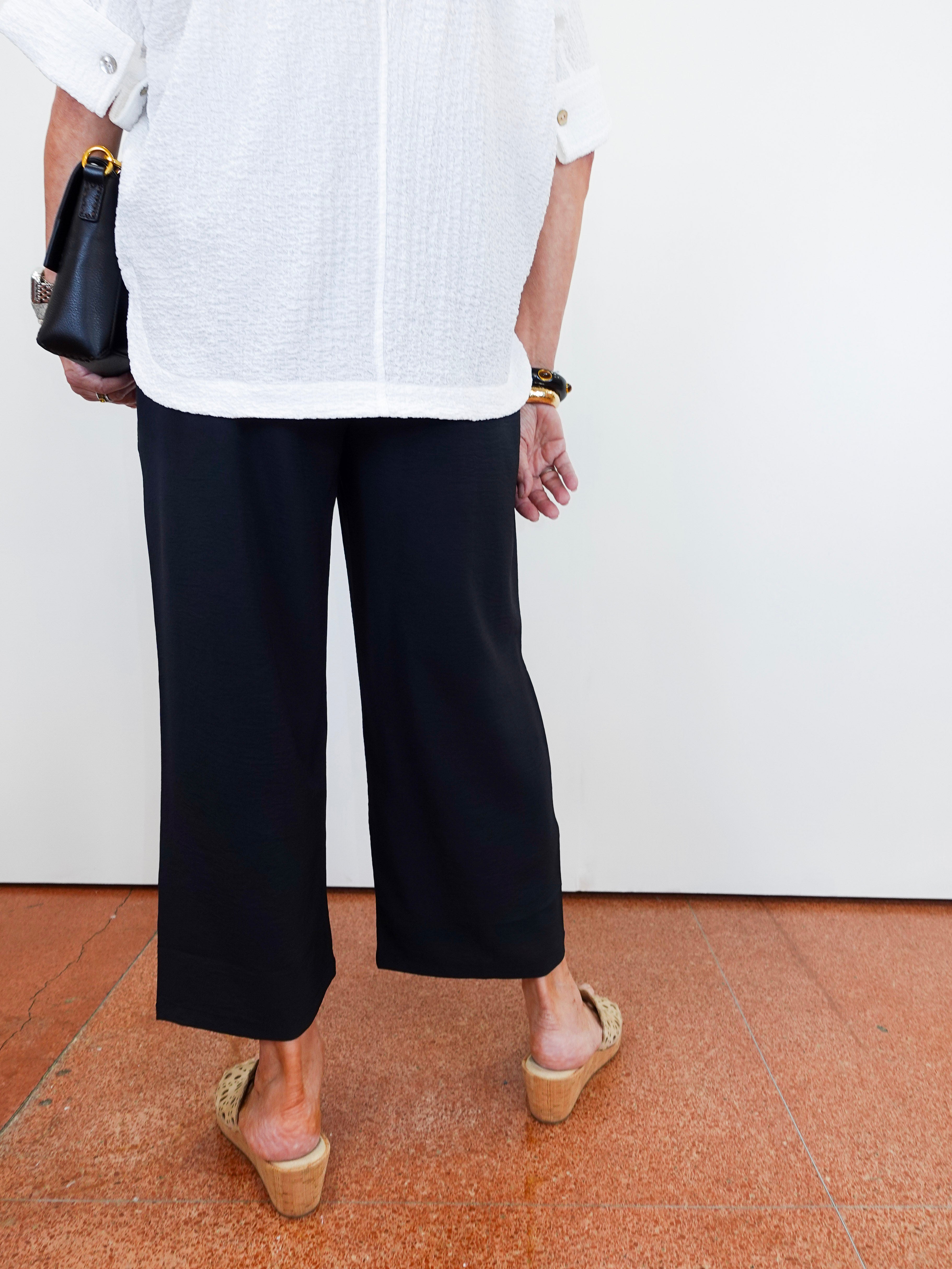 Person wearing a white shirt, black pants, and beige sandals on a plain background