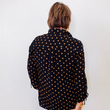 Person wearing a black polka dot shirt against a white wall