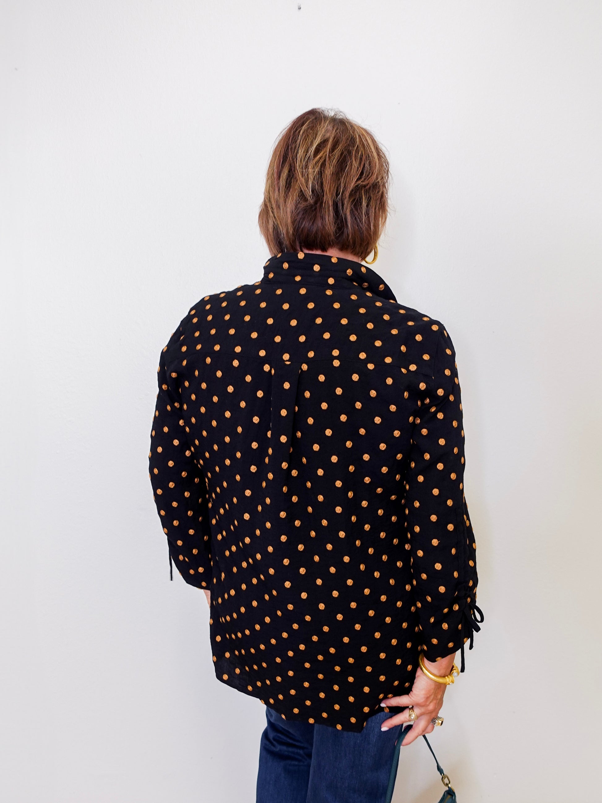 Person wearing a black polka dot shirt against a white wall
