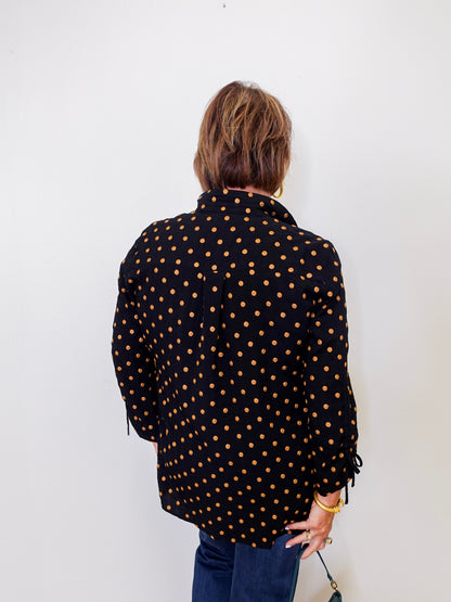 Person wearing a black polka dot shirt against a white wall
