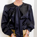 Person wearing a black blouse with a tie neckline against a white background